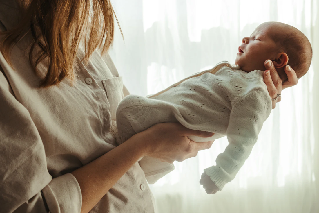 Une maman tenant son nouveau-né dans ses bras, dans la lumière d’une fenêtre