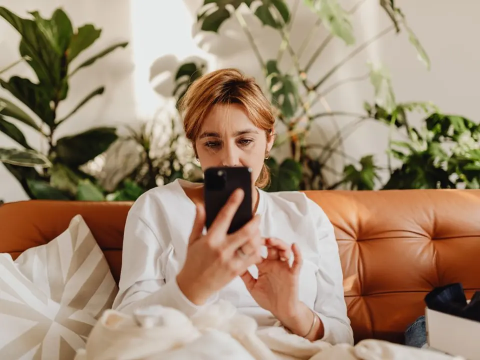 Une femme échange sur son téléphone, installée dans son canapé