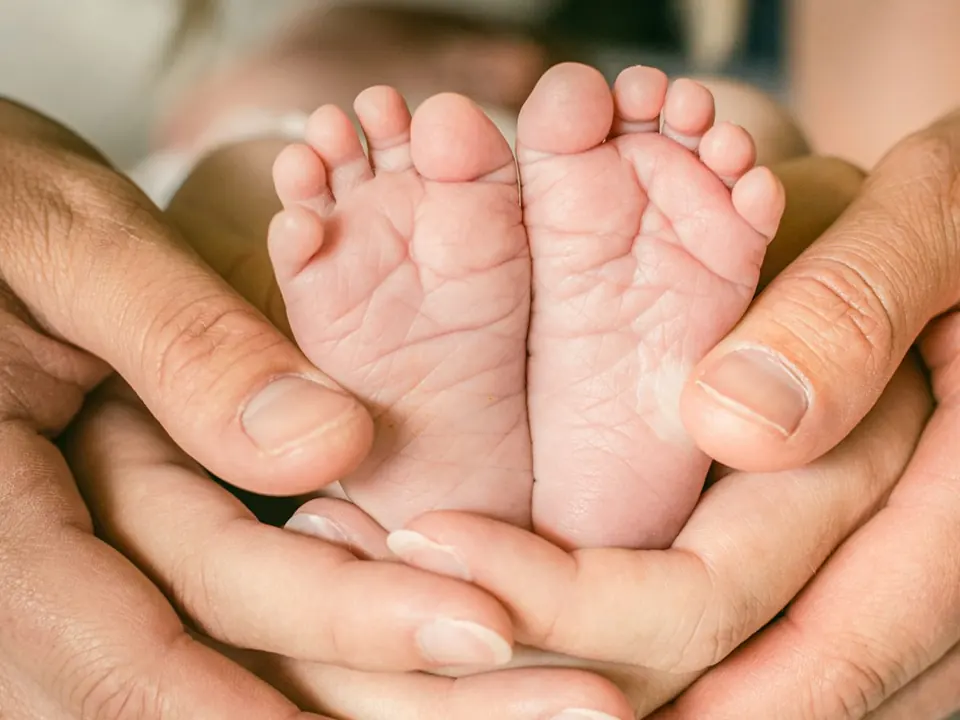 Les petits pieds d’un bébé délicatement entourés par des mains adultes